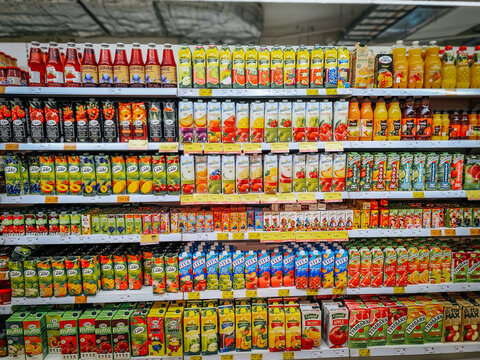 A well-organized supermarket shelf displaying a colorful assortment of fruit juices in cartons and bottles. The variety includes apple, orange, and berry flavors. 