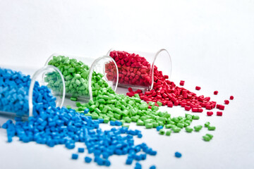 Blue, green and red masterbatch granules spilled from measuring cup, isolated on white background....