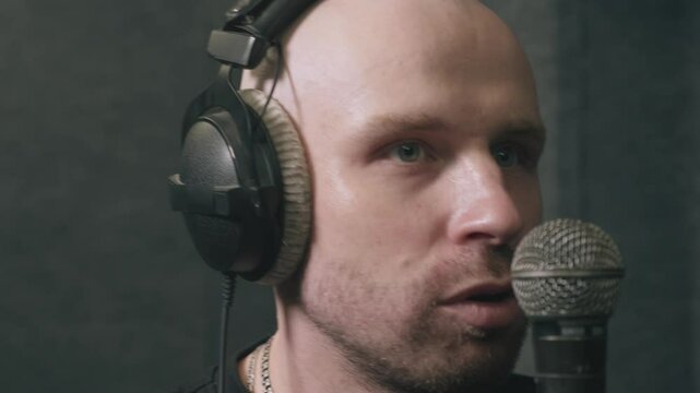 Hip-hop artist putting on headphones and getting ready to rap in professional recording studio. Focused musician preparing to deliver powerful vocals into microphone.
