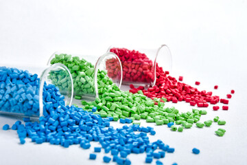 Blue, green and red masterbatch granules spilled from measuring cup, isolated on white background....