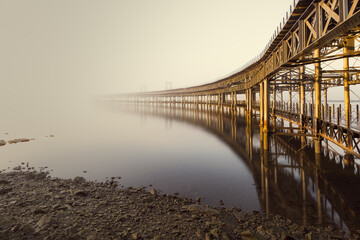 Warm view of the Riotinto mining company hiscorical dock in Huelva, Spain, covered by fog, with silky water and reflections.
