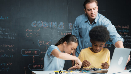 Caucasian teacher talking about electric tool while student fixing robotic model on table with...