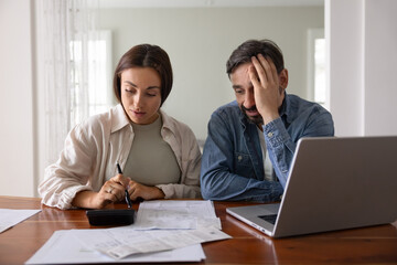 Concerned young middle aged couple counting expenses, finding overspending, money loss, risk of...