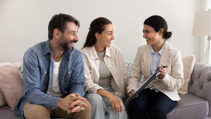 Happy Indian consultant, adviser, agent meeting with couple of customers at home, showing paper agreement, explaining good terms, giving for signing after consultation