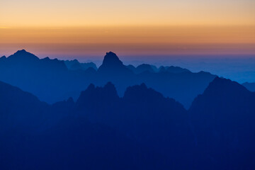 Sunset silhouette of the mountains in the Alps. Dolomites alpine beautiful landscape in red, orange and yellow light of sunset and sunrise, dawn soft light through darkness of the sky in the Dolomiti