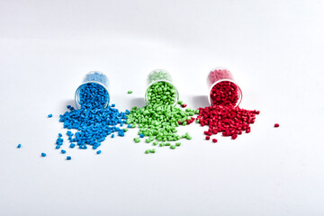 Blue, green and red masterbatch granules spilled from measuring cup, isolated on white background....