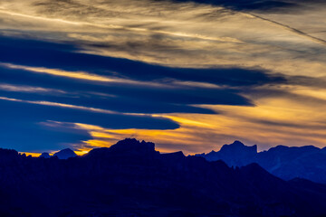 Sunset silhouette of the mountains in the Alps. Dolomites alpine beautiful landscape in red, orange and yellow light of sunset and sunrise, dawn soft light through darkness of the sky in the Dolomiti
