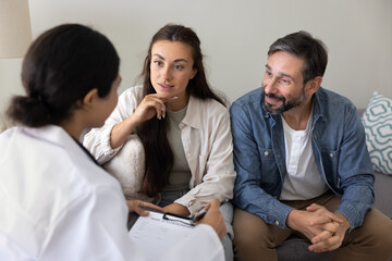 Positive young middle aged couple consulting about healthcare with doctor woman, planning...