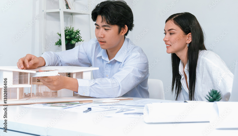 Poster professional male asian architect using ruler to measure house model length while young beautiful ca