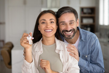 Happy Latin couple of homeowners showing key from new home, looking at camera for portrait, smiling, celebrating real estate property buying, getting affordable house