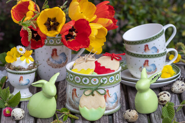 Oster-Tischdekoration mit Keksen, Tulpenstrauß und Geschirr mit Ostermotiv	