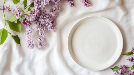 On a flat surface of a white tablecloth lies a white modern dinnerware set with beautiful flowers
