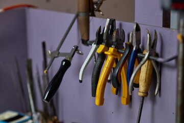 Various hand tools hanging neatly on hooks in an organized workshop setup with purple walls and a...