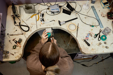 Individual working at cluttered workbench with various tools scattered around in a workshop...