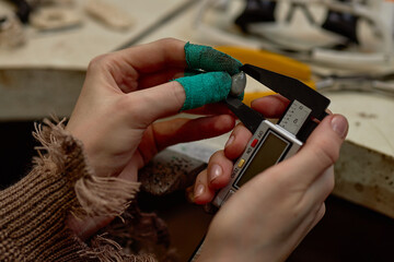 Close-up of hands holding digital caliper and measuring an object in workshop environment. Detailed...