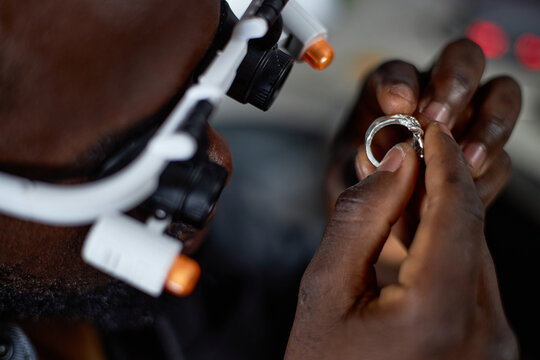 Close-up of person inspecting a piece of jewelry using a magnifying headset device. Detailed focus on hands and jewelry, showcasing precision and careful examination