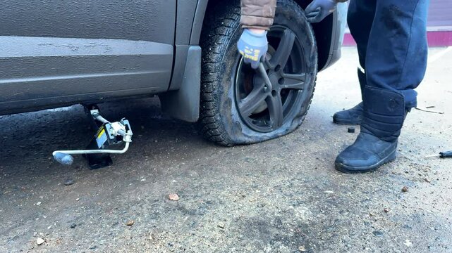 man unscrews a flat tire on a car