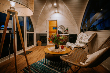 Cozy wooden cabin interior with wicker chairs, a rustic coffee table, a fireplace, and warm lighting, creating a relaxing and inviting ambiance.