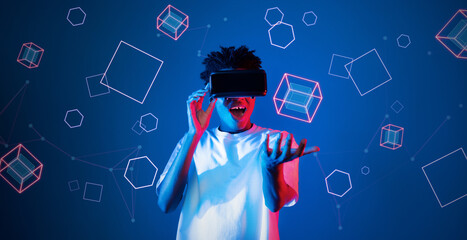 Smart boy standing at blue background while floating geometric shape. African man playing game and wearing VR goggle and casual shirt. Augmented reality technology innovation concept. Ingenuity.