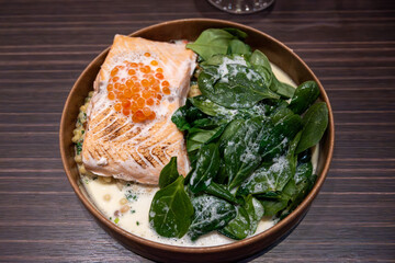 Portion of grilled wild scottish salmon served with green spinach and white cream sauce and red caviar