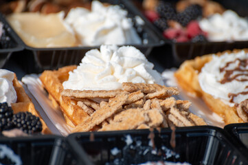 Variety of fresh baked waffles richly decorated with different toppings, sweet sweets, chocolate, cream, fruit and berries, jelly sweets in bakery with confectionery shop, old Volendam, Dutch sweets