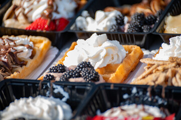 Variety of fresh baked waffles richly decorated with different toppings, sweet sweets, chocolate, cream, fruit and berries, jelly sweets in bakery with confectionery shop, old Volendam, Dutch sweets