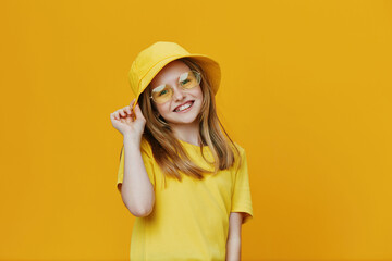 Cheerful girl in yellow attire with sunglasses, posing against a bright yellow background,...