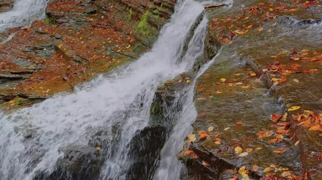 Crisp 4K footage of a cascading waterfall with brilliant autumn leaves at Buttermilk Falls State Park, perfect for nature lovers and stock users.