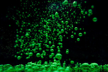 Green bubbles rise in a dark underwater environment creating a stunning visual display
