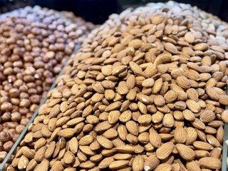 The kernels of peeled hazelnuts and roasted almonds on the counter at the market, put up for sale at supermarket's nut stand, showcases organic products, vegetarian food, and healthy food. Close-up