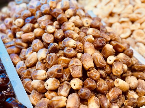 Ripe dark dates are laid out on a tray for sale in a supermarket with an emphasis on the rich quality and color of dried fruits. Close-up