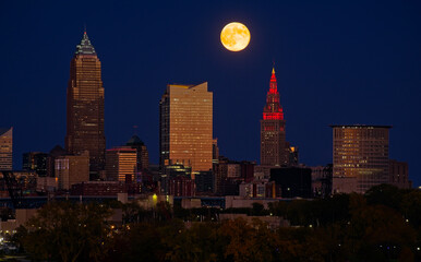The full moon of October 17, 2024, rises above and between towers over downtown Cleveland Ohio.