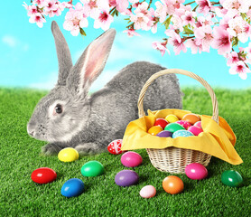 Easter celebration. Cute fluffy rabbit and colorful eggs on green grass under blooming tree