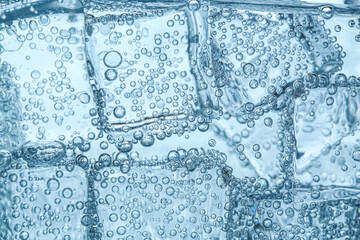 Refreshing soda water with ice cubes as background, closeup