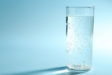 Soda water in glass on light blue background, space for text