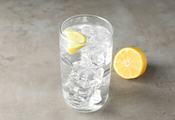 Refreshing soda water with ice cubes in glass and cut lemon on grey textured table, closeup