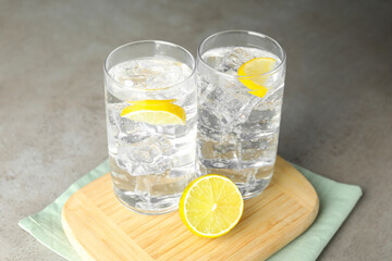 Refreshing soda water with ice cubes and cut lemon in glasses on grey textured table, closeup