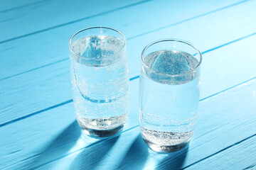 Refreshing soda water in glasses on light blue wooden table, closeup