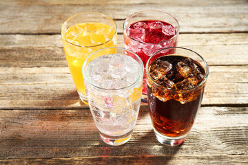 Soda water of different flavors with ice cubes in glasses on wooden table, closeup