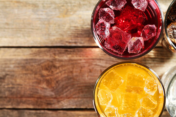 Soda water of different flavors with ice cubes in glasses on wooden table, top view. Space for text