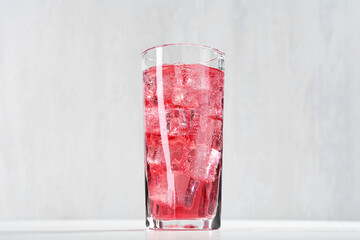 Sweet soda water with ice cubes in glass on white table, closeup