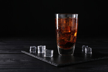 Sweet soda water in glass with ice cubes on black wooden table, space for text