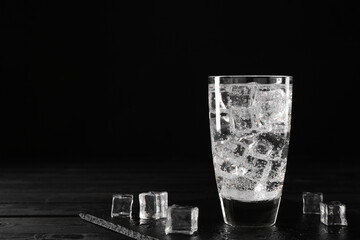 Refreshing soda water in glass with ice cubes on black wooden table, space for text