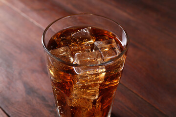 Sweet soda water with ice cubes in glass on wooden table, closeup