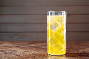 Sweet soda water with ice cubes in glass on wooden table, space for text