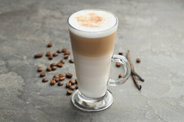 Tasty latte macchiato in glass cup, coffee beans and vanilla pods on grey table, closeup