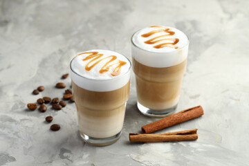 Tasty latte macchiato in glasses, coffee beans and cinnamon on grey table, closeup