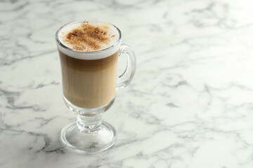 Tasty latte macchiato in glass cup on white marble table, closeup. Space for text