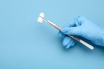 Doctor holding surgical tweezers with gauze on light blue background, closeup. Space for text