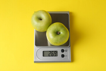 Electronic kitchen scale with apples on yellow background, top view
